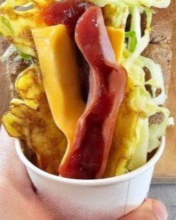 Un sándwich de estilo callejero coreano servido en un vaso de papel, con huevo, repollo, queso y salsa.